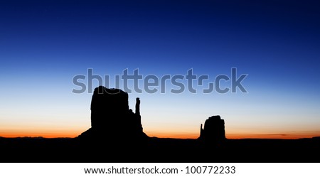 A colorful sunrise silhouette photograph of the East and West Mitten Buttes in the Monument Valley region of the Colorado Plateau that spans the northern border of Arizona and southern border of Utah.
