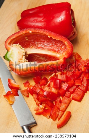 A fresh red bell pepper vegetable diced while resting on a wood cutting board