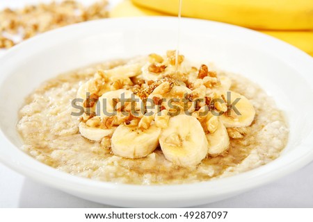 A bowl of oatmeal with bananas and nuts and honey being drizzled over it