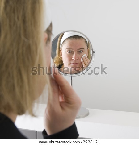 cleaning her face, reflection in the bathroom mirror