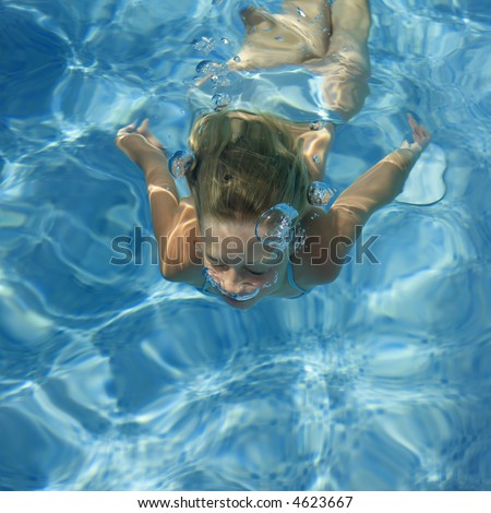 girl swimming under water in a swimming pool, breathing out with air bubbles
