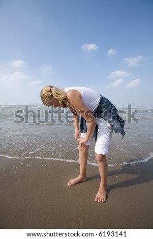 girl rolling up her pants for a walk along the beach