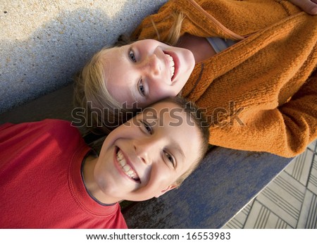 brother and sister lying down on a bench, laughing and looking at the camera