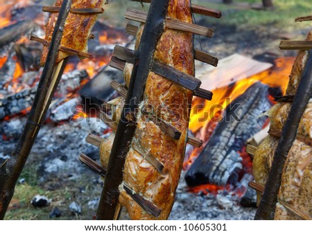 Salmon cooking and smoking on sticks next to a fire.