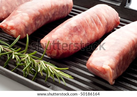 raw sausage with rosemary over grill focus on the second sausage