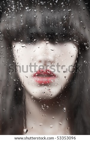 Closeup portrait of brunette woman behind the glass with water drops on it