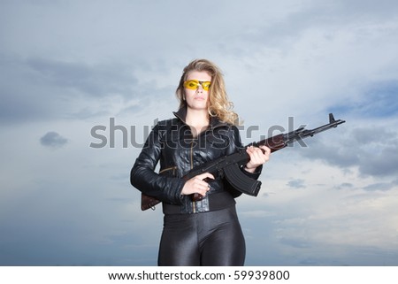 Blonde beautiful woman on the roof in yellow glasses holding weapon
