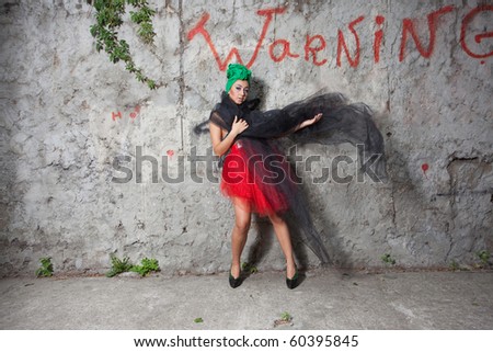 Model with green scarf on head and red tulle skirt posing near the wall