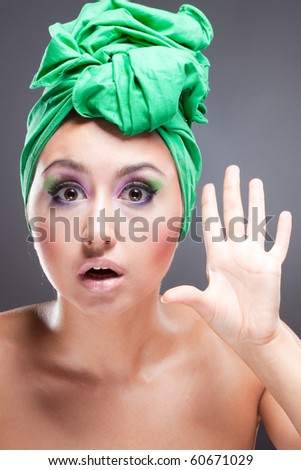 Scared woman with green scarf on head and bright pink-green makeup rejecting