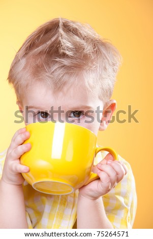 Funny boy drink from big yellow cup looking at camera