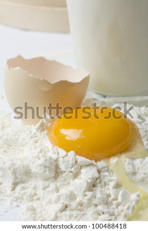 Yellow raw egg yolk on flour with glass of milk