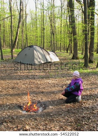 Camp in the forest. Cold morning in the spring forest. Single girl at the camp fire.