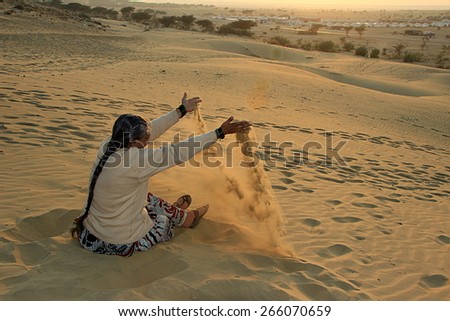 Indian lady enjoying dropping smooth and fine sand at sunset at Sam Sand Dunes, Jaisalmer, Rajasthan, India, Asia