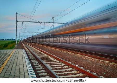 Railroad travel and transportation industry business concept: summer night view of high speed passenger train departing from railway station platform with motion blur effect