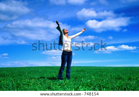 Girl reaches out to the sky on a grass field.