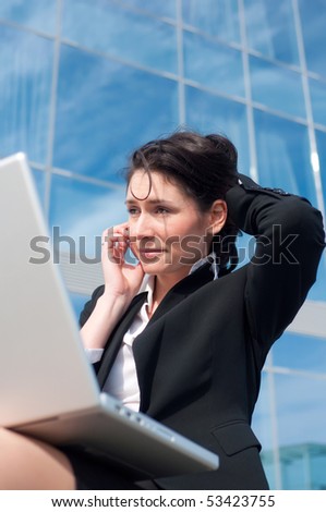Business woman in black suit with a laptop speaking by a phone