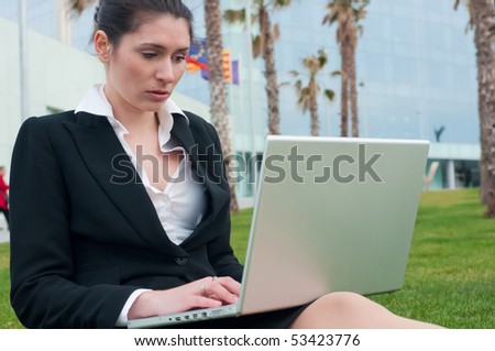 Business woman in black suit with a laptop sitting on the grass