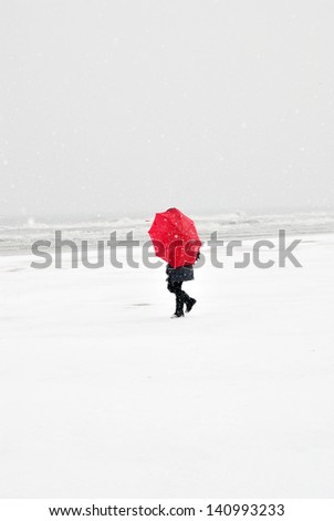 person on the beach with red umbrella in snow storm