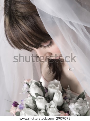 Brunette bride looking down at her bouquet, focus on her eyes and hair, soft focus on the flowers
