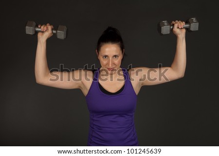 Studio shot of a fit brunette woman lifting weights on a grey background