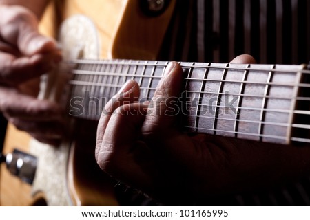 Close up shot of a man with his fingers on the frets of a guitar playing