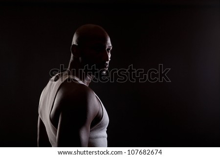 Strong contrast shot of  a young, handsome, muscular black man in shadows.