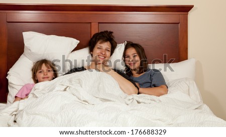 Shots of a mother and her two daughters waking up in bed with white linens part of a series