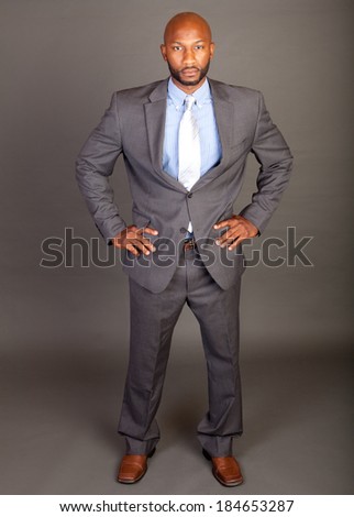 Portrait of a handsome young African American business man with a shaved head looking right at the camera with his hands on his hips in a confident pose