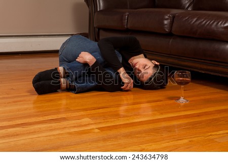 Young woman lying on the floor passed out in the fetal position with a wine glass