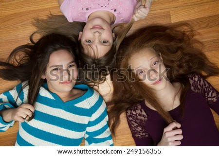 Three young, diverse  girls  lying on a wood floor looking up at the camera. One African American with red hair, one hispanic and one caucasian