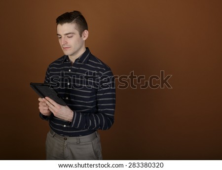 Nice shot of a young man using a tablet in a casual outfit on a brown background with room for copy