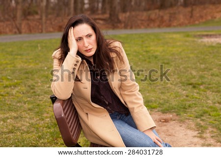 Sad woman sitting on a bench on a cloudy day with a coat looking lonely