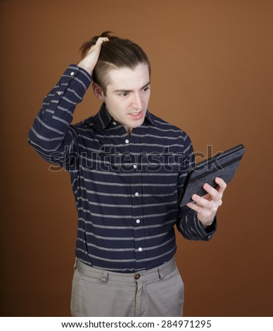 Nice shot of a young man using a tablet reacting to the content in a casual outfit on a brown background with room for copy