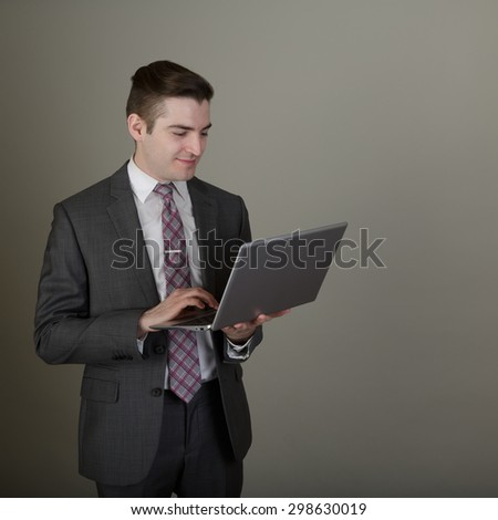 Studio shot of a young business man in a suite posing in the studio on a light grey background with a stylish haircut holding a laptop