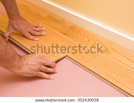 Series of shots of engineered hardwood floor being installed by a worker over pink felt paper using hand tools