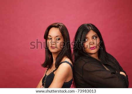 Hispanic and Indian girl in the studio standing back to back looking like they are about to fight