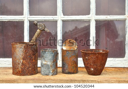 Rusty old tin cans used for tools in front of an old window.