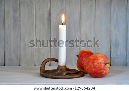 Candle in a handmade candle stick and two red apples in a sparse composition.