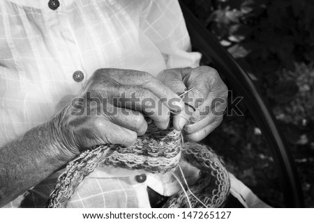 Closeup of old wrinkled hands knitting. Black and white.