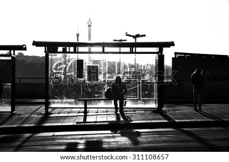 Street photography of someone waiting at a bus stop in black and white.