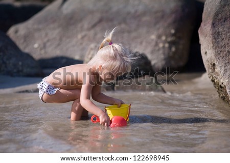 Pretty little girl playing with toys and water near rocks in the ocean