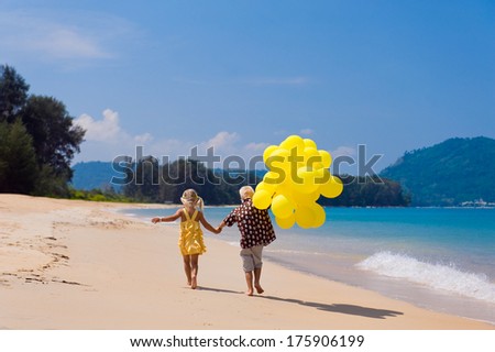Back view of two kids with yellow balloons running at the beach