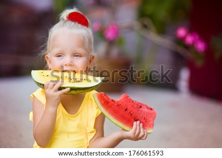 Cute little girl in yellow swimming suit eating red and yellow watermelon