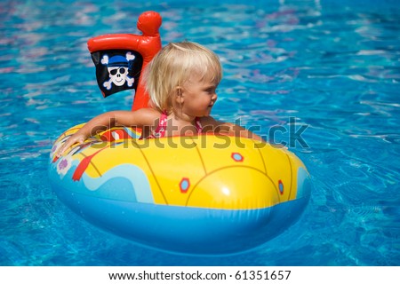 Baby girl sitting in the inflatable boat in the swimming pool.