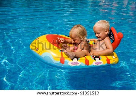 Brother and sister sitting in the inflatable boat in the swimming pool.