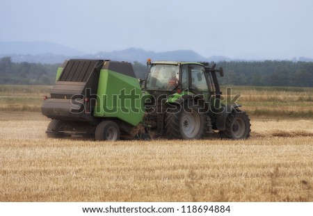 Tractor collecting hay on the summer field.