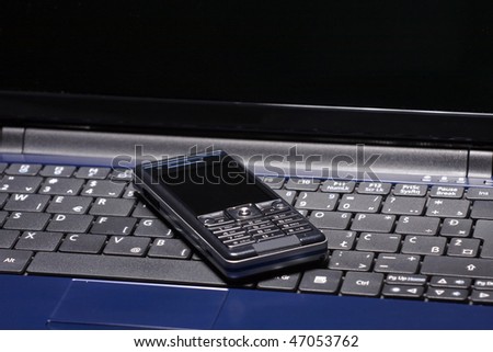 Blue laptop computer with mobile phone on keyboard.