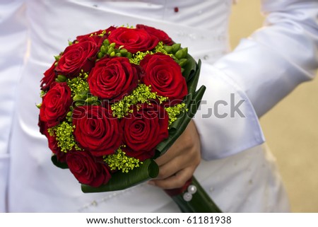 Closeup of the bride holding a bouquet of red roses.