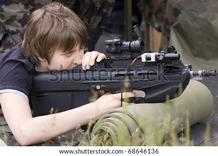 Teenage boy aiming with the modern military assault rifle.