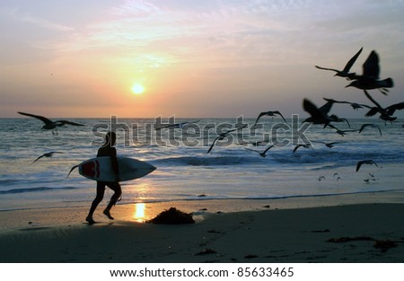 Surfer running on the beach with sunset in the background.